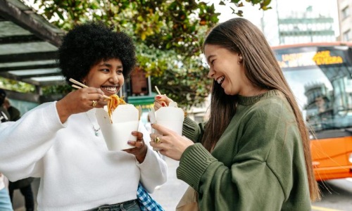 Two women laughing and eating street food in the city.